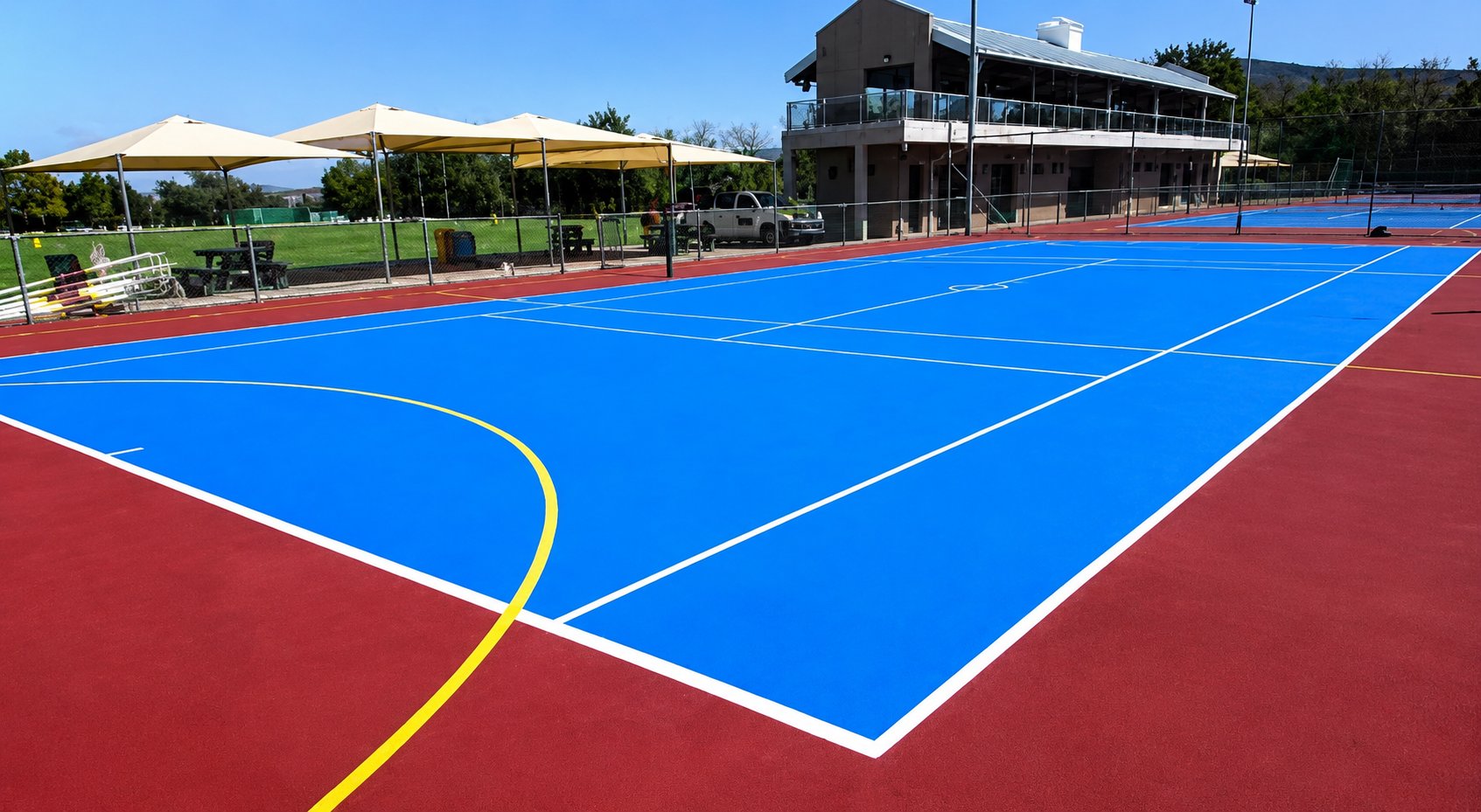 Blue acrylic tennis court with red surrounds and netball markings
